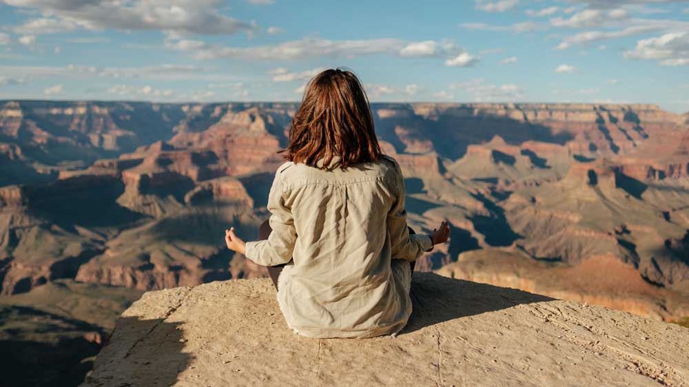 Woman seated in a natural setting, engaged in mindfulness breathing exercises.