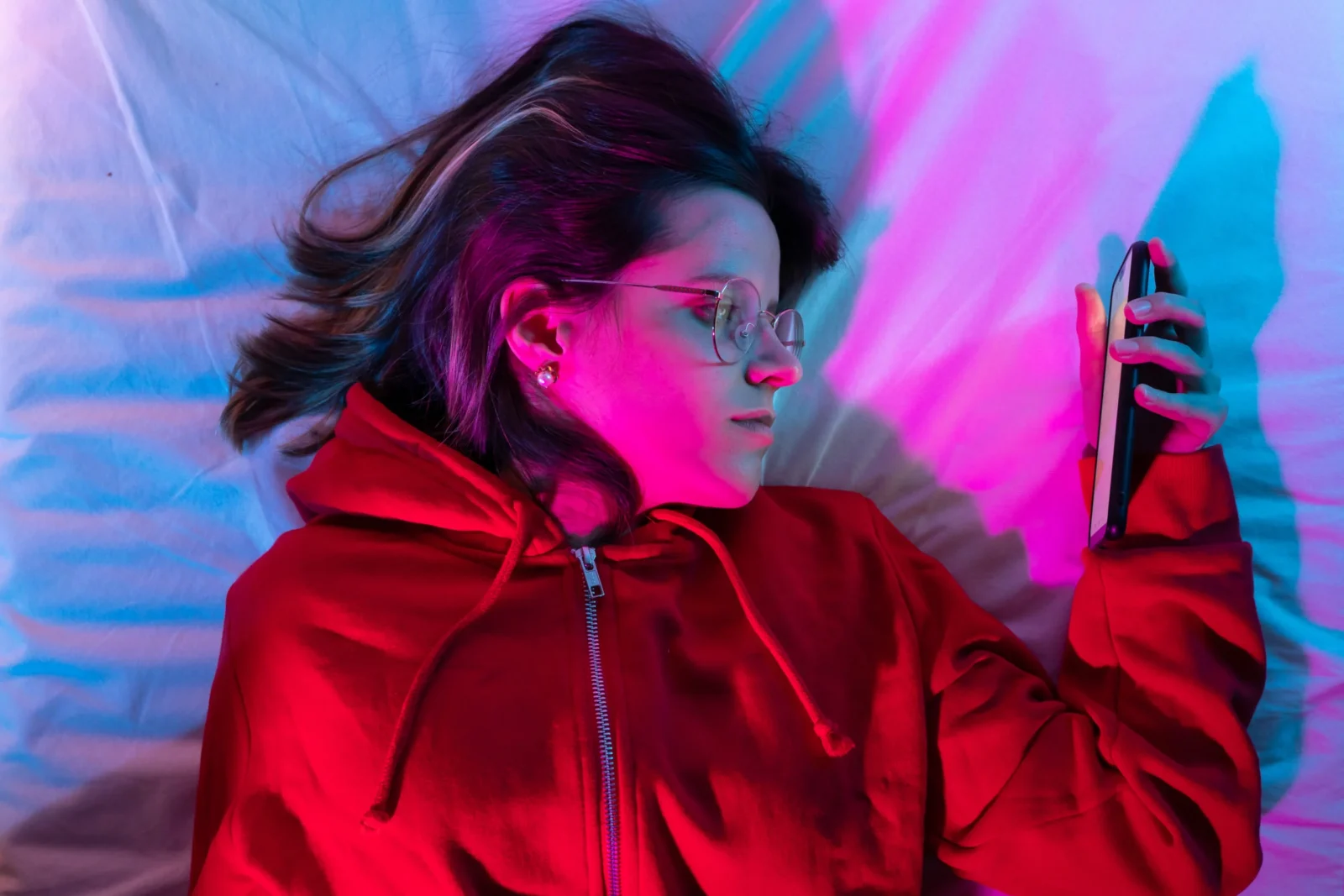Social-Media-Affects Your-Mental-Health A woman lays in bed, zoned out while staring at her phone, depicting the potential negative consequences of social media use on mental well-being.