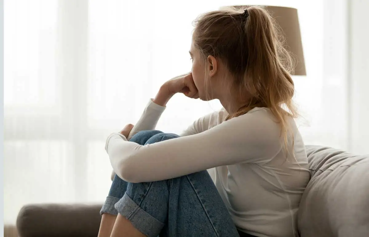 Sad teenager sitting and looking out of a window, symbolizing teen depression.