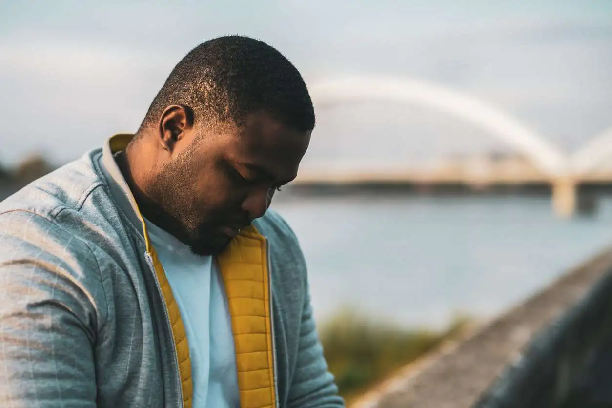 Severely depressed man sitting outside by the water